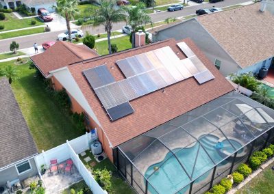 Solar panels installed on a residential red-shingle roof, with a screened-in pool and backyard patio in a suburban neighborhood setting.