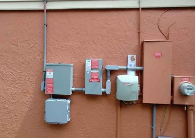 Solar energy electrical components, including inverters and utility connections, mounted on an orange residential exterior wall.