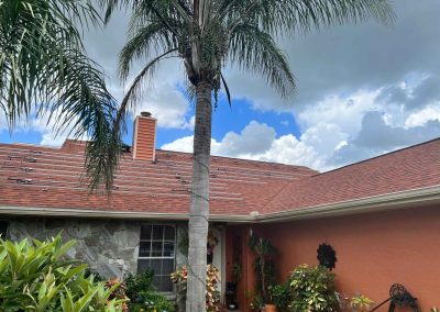 Residential roof ready for solar panels, featuring mounting brackets, palm trees, and vibrant landscaping against a cloudy sky.