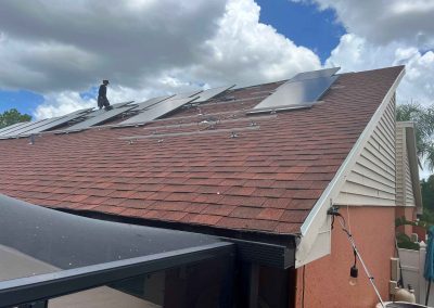 Technician installing solar panels on a residential roof with mounting rails and partially secured panels under a cloudy sky.