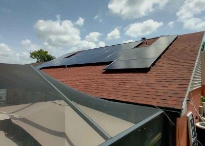 Solar panels installed on a red-shingle residential roof, with a screened patio enclosure and clear blue skies in the background.