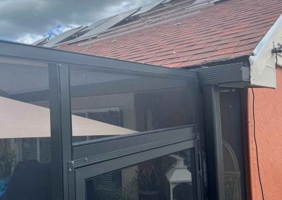 Partially installed solar panels on a residential roof with mounting hardware, next to a screened patio area under a cloudy sky.