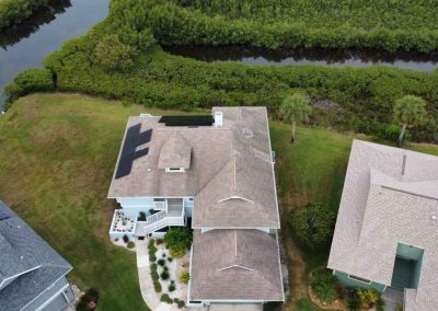 Aerial view of a coastal home with solar panels installed on the roof, surrounded by greenery and a waterway.